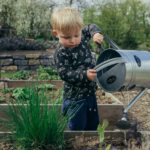 boy in black and white long sleeve shirt standing beside gray metal watering can during daytime