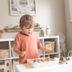 boy in orange crew neck t-shirt standing in front of white wooden table with cupcakes